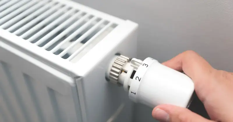 Dłoń kręci termostatem grzejnika, ustawiając temperaturę. To znak, że zbliża się czas, kiedy zaczyna się sezon grzewczy.